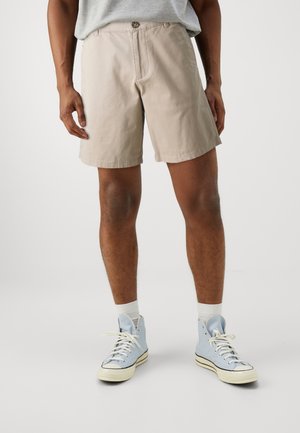 Beige Baumwollshorts mit Knopfverschluss, mit einem lockeren Schnitt und Seitentaschen, kombiniert mit hellblauen High-Top-Sneakern.