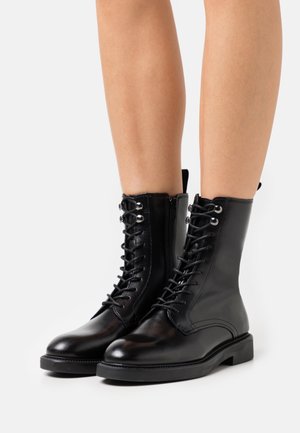 Czarne skórzane botki za kostkę z przodem na sznurowadła i srebrnymi przelotkami, gładką teksturą, zaokrąglonym noskiem oraz płaską gumową podeszwą.