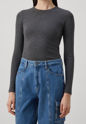 Top gris de manga larga con un diseño ajustado y textura acanalada, combinado con pantalones vaqueros azules sueltos que cuentan con un bolsillo lateral.