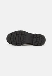 Semelle en caoutchouc noir avec un motif de rainure texturé, dotée d'un talon lisse et de rainures marquées pour une meilleure traction.