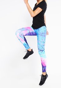 Färgglada leggings med ett blått och rosa abstrakt mönster, som har ett lövmotiv och geometriska detaljer. Bärs med en svart t-shirt med kort ärm och svarta sneakers.