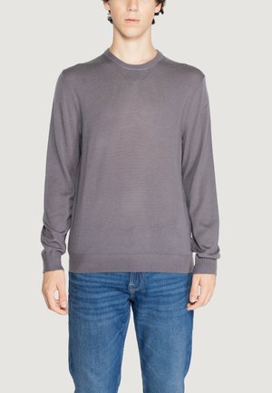 Suéter gris de punto con mangas largas, puños y dobladillo acanalados, con un escote redondo y un sutil patrón texturizado. Llevado sobre unos jeans azules.