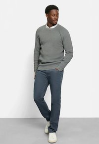 Gray knit sweater with round neckline, single ribbed texture. Paired with dark blue pants and light-colored sneakers. Casual outfit.