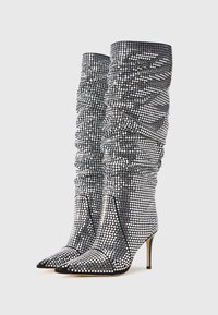 Cizme negre până la genunchi, cu vârf ascuțit, decorate cu rhinestones argintii în design plisat, având un toc înalt și subțire.