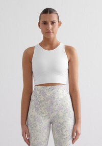 Witte sportieve crop top met een ronde halslijn en mouwloos ontwerp, gecombineerd met hoge taille leggings met een pastelkleurig bloemenpatroon.