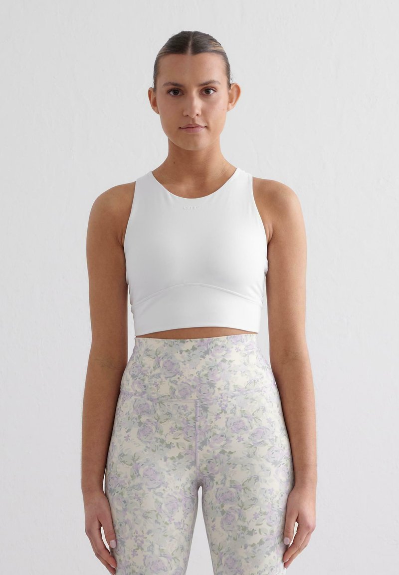 Witte sportieve crop top met een ronde halslijn en mouwloos ontwerp, gecombineerd met hoge taille leggings met een pastelkleurig bloemenpatroon.
