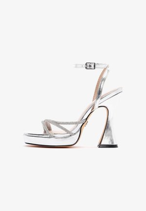 Silver high-heeled sandal with wide platform, rhinestone crisscross straps, ankle strap with buckle, and flared block heel.