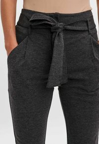 Šedé kalhoty z jemné tkaniny, s uvázaným pasem, šikmými bočními kapsami a uvolněným střihem.