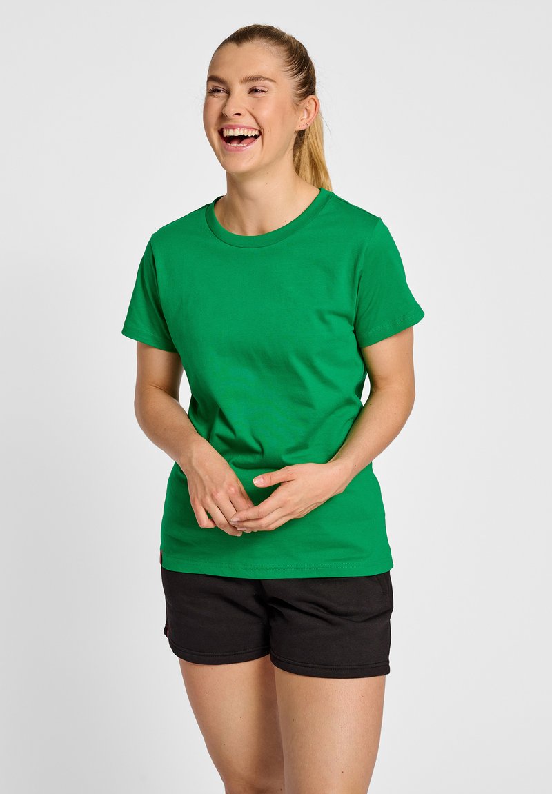 Grøn bomulds t-shirt med rund halsudskæring og korte ærmer, parret med sorte shorts. Har en glat tekstur uden synlige mønstre.