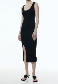 Svart ribbad midiklänning med en rundad halsringning, som har en slits på sidan. Slät textur, åtsittande design och utan ärmar.
