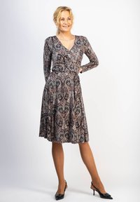 Pitkähihainen, istuva mekko tummasta kankaasta, jossa on paisley-kuvio mustana, valkoisena ja ruosteenvärisenä; levenevä hameosa; v-mallinen kaula-aukko.