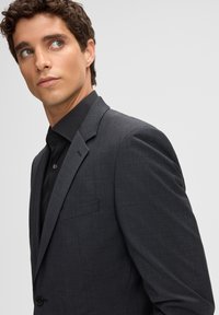 Grijze, gestructureerde blazer met een gesneden revers en één knoopsluiting, gecombineerd met een zwart overhemd met kraag.