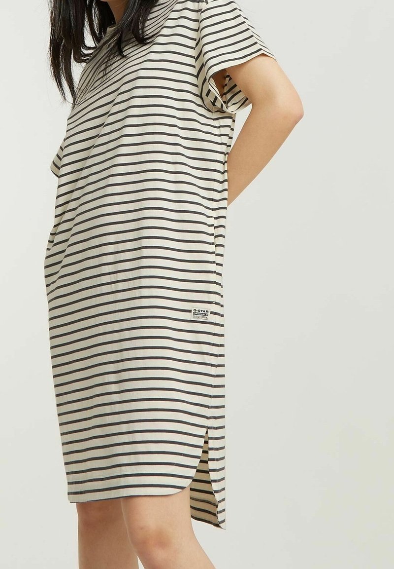 Sukienka w paski w kolorze kremowym i ciemnoszarym. Krótkie rękawy, luźny krój, rozcięcia po bokach oraz mała naszywka z logo na dole. Miękka tekstura tkaniny.