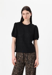 Zwart T-shirt met korte mouwen en pofmouwen, met een textuur van kant en een ronde halslijn. Gecombineerd met brede broek in leoprint.