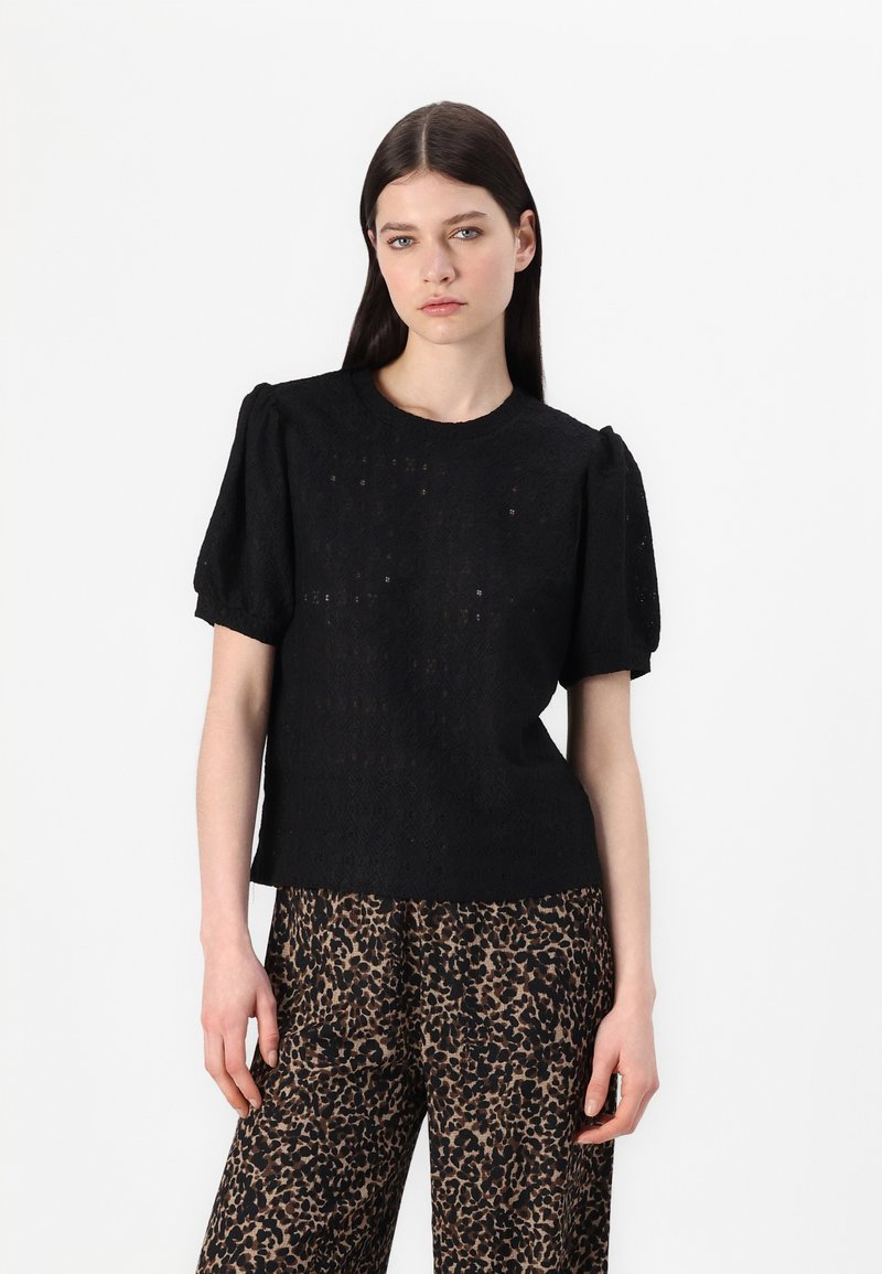 Zwart T-shirt met korte mouwen en pofmouwen, met een textuur van kant en een ronde halslijn. Gecombineerd met brede broek in leoprint.