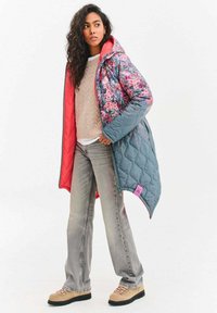 Prešívaný dlhý kabát v modrej farbe s kvetinovým vzorom, ružovými akcentmi a kapucňou. Kombinovaný s béžovým pleteným svetríkom a svetlosivými džínsami.