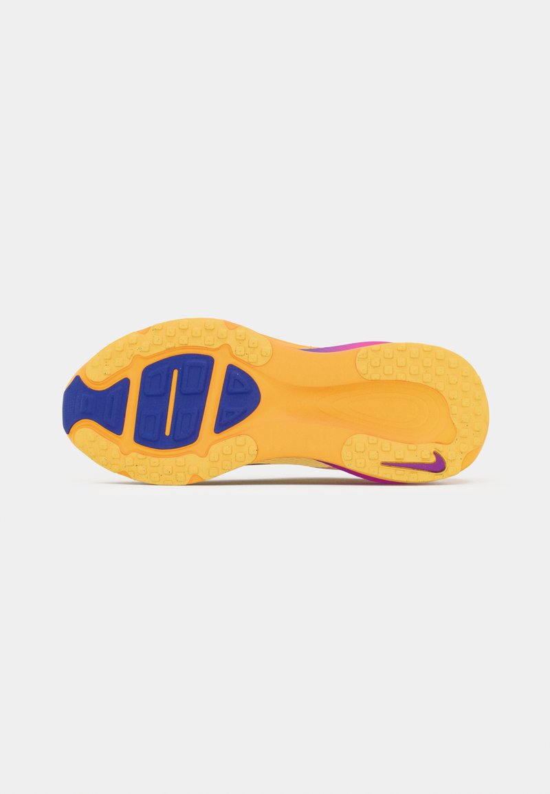 Suela de zapato con caucho amarillo texturizado, detalles en púrpura y un diseño segmentado con surcos y un logotipo grande en el talón.