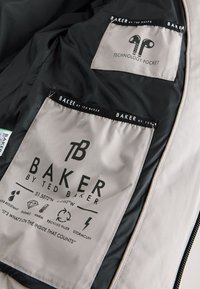 Leichte Jackeninnenseite mit schwarzem Futter. Enthält zwei beschriftete Taschen: eine für Technik und eine mit Pflegehinweisen und Symbolen.