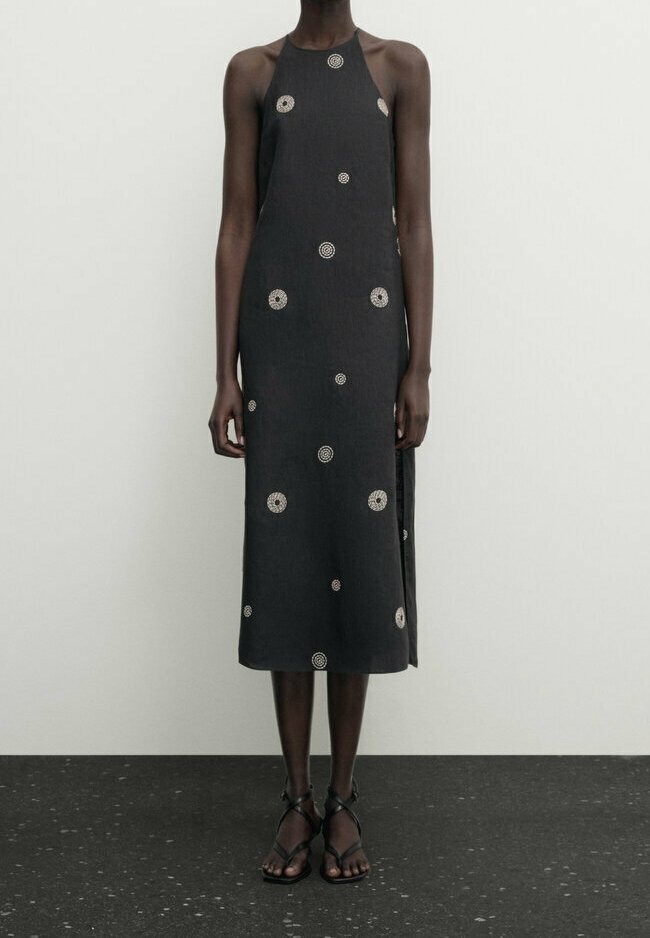 Robe noire à col halter avec broderie circulaire blanche. Mi-longue, coupe ample, en tissu léger, avec fentes latérales et design simple.