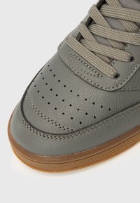 Grå lær-sneaker med perforert tåområde og teksturert overflate. Har flate lisser, sydd detaljering og en såle i gummigummi.