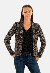 Blazer noir avec un motif texturé multicolore. Présente une coupe ajustée, des revers crantés, et est porté sur une chemise noire à pois.