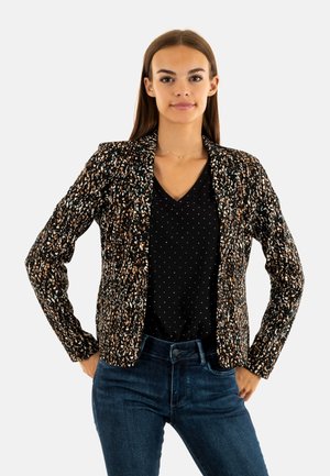 Blazer noir avec un motif texturé multicolore. Présente une coupe ajustée, des revers crantés, et est porté sur une chemise noire à pois.
