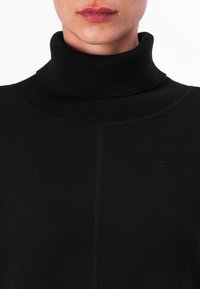 Juoda šiltinė megztinė su aukštu kaklu, pagaminta iš megztos medžiagos, su vientisu dizainu ir tekstūruotu raštu.