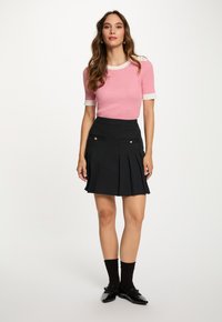 Haut en tricot rayé rouge et blanc à manches courtes, associé à une jupe plissée à rayures noires avec des poches à boutons dorés. Chaussettes et chaussures noires.