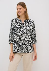 Svart och vit leopardmönstrad blus med långa ärmar och en partiell knappslå, matchad med ljusbeiga byxor. Slät tygertextur.