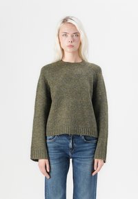 Oliwkowy sweter z dzianiny z okrągłym wycięciem i długimi rękawami, charakteryzujący się teksturowanym materiałem i skróconym dołem. Połączony z niebieskimi dżinsami.