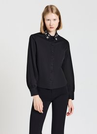 Schwarze Hemdbluse mit langen Ärmeln, verzierten Kragen mit weißen Blumenmustern, glattem Stoff, tailliertem Schnitt und abgerundetem Saum.