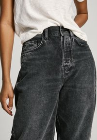 Juodos džinsinės kelnės su aukštu liemeniu, tiesių kojų, su subtiliu blukimu ir penkių kišenių dizainu. derinamos su šviesios spalvos, laisvo kirpimo marškinėliais.