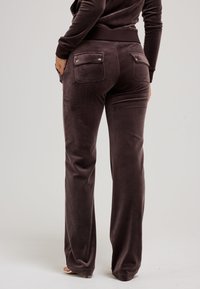 Bruine fluwelen broek met een gladde textuur, voorzien van twee achterzakken met knoopsluitingen. Het ontwerp heeft rechte pijpen en is vol lengte.