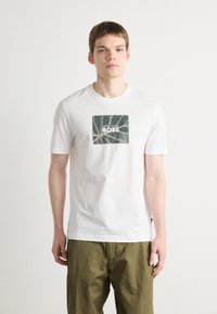 Bílý bavlněný tričko s čtvercovou grafikou a designem zeleného listu a slovem "BOSS" tučnými bílými písmeny. Krátké rukávy, kulatý výstřih.