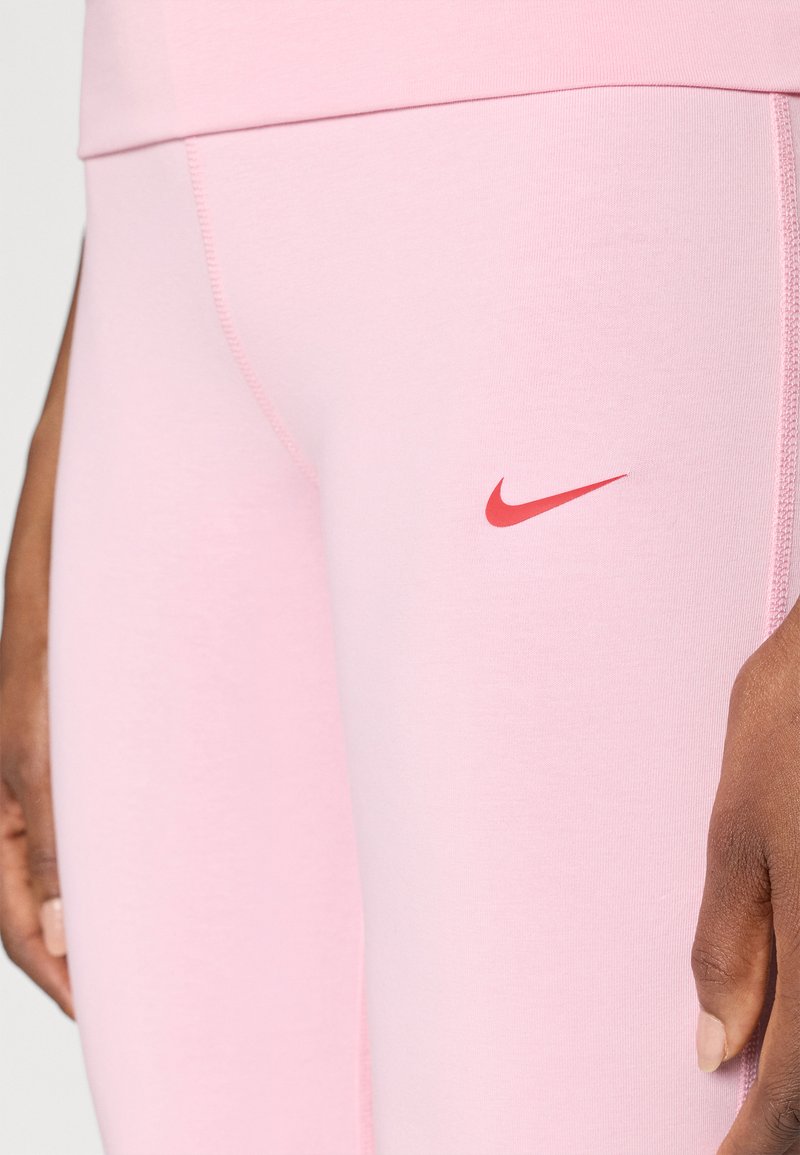 Leggings rosa realizzati in materiale elastico, con una superficie texturizzata e un logo Nike rosso sulla coscia sinistra.