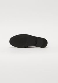 Svart skosåle med en teksturert gummioverflate, som har en glatt front og et mønstrete grepdesign, som gir trekkraft og holdbarhet.