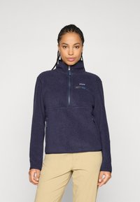 Navy blue fleece pullover with a zippered neck, textured exterior, chest pocket, and side pockets, featuring a brand logo on the left chest.