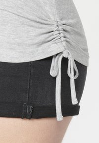 Šedý vrchný diel s zaobleným lemom, s detailmi šnúrky po stranách. Čierne denimové šortky s čistým lemom a minimálnym šitím.