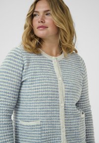 Light blue and white striped cardigan made of soft material, featuring a round neck, button closure, and two front pockets.