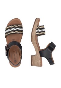 Black and tan sandals with a woven striped strap featuring white, black, and gold threads. Chunky, textured wooden heel. Adjustable strap detail.