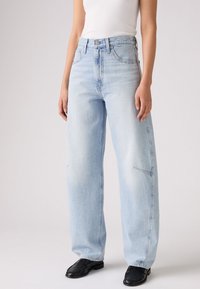 Jeans ampi blu chiaro con vita alta, realizzati in denim, dotati di tasche frontali e finitura sbiadita. Abbinati a un top aderente bianco.