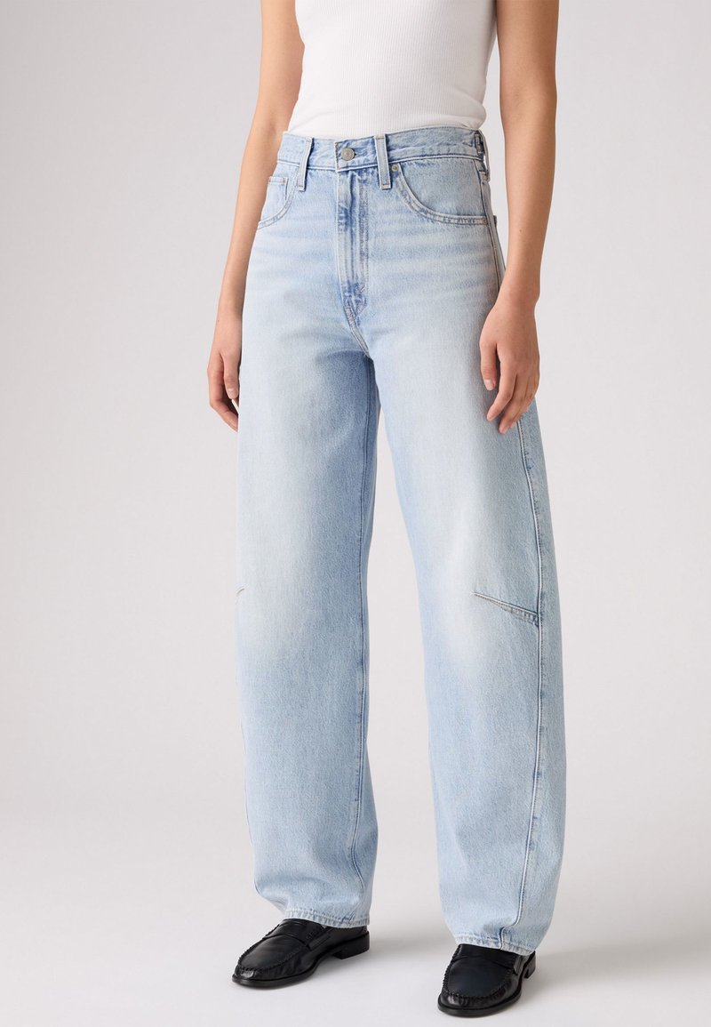 Jeans ampi blu chiaro con vita alta, realizzati in denim, dotati di tasche frontali e finitura sbiadita. Abbinati a un top aderente bianco.