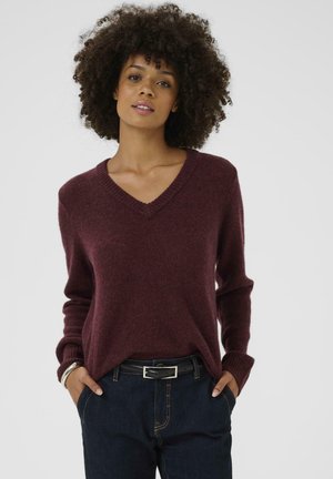 Burgundy v-neck neule joka on pehmeää neulosta, pitkähihaiset ja rento leikkaus. Yhdistetty tummansiniset farkut ja musta vyö.