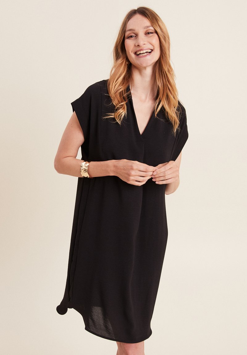 Vestito nero fino al ginocchio con scollatura a V, maniche corte e vestibilità morbida. Realizzato in un materiale soffice, presenta una leggera caduta e tasche laterali.