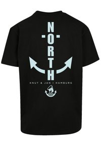 Black cotton t-shirt featuring light blue graphic text "NORTH" with arrows and "KNUT & JAN | HAMBURG" above an anchor and waves design.