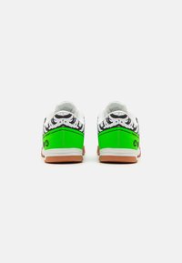 Białe sneakersy z zieloną bazą, czarno-białym wzorem tygrysa na pięcie i bokach oraz brązowymi gumowymi podeszwami. Cechują się minimalnym oznakowaniem.