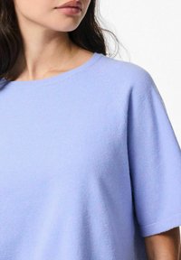 Gai zils īsām piedurknēm džemperis ar apaļu kakla izgriezumu un raglanu piedurknēm, izgatavots no mīksta materiāla ar gludu tekstūru.