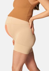 Pantaloni shorts premaman beige con una texture liscia e un'alta vita, caratterizzati da un accento rosa sulla parte posteriore e un design aderente per il supporto.