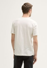 Lichtbeige T-shirt met korte mouwen, een zachte uitstraling, een ronde halslijn en een rechte achterkant, gecombineerd met zwarte broeken.