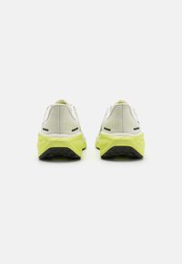Baskets blanches et gris clair avec une tige en maille respirante, une semelle extérieure jaune vif et des accents noirs sur le talon et les côtés.